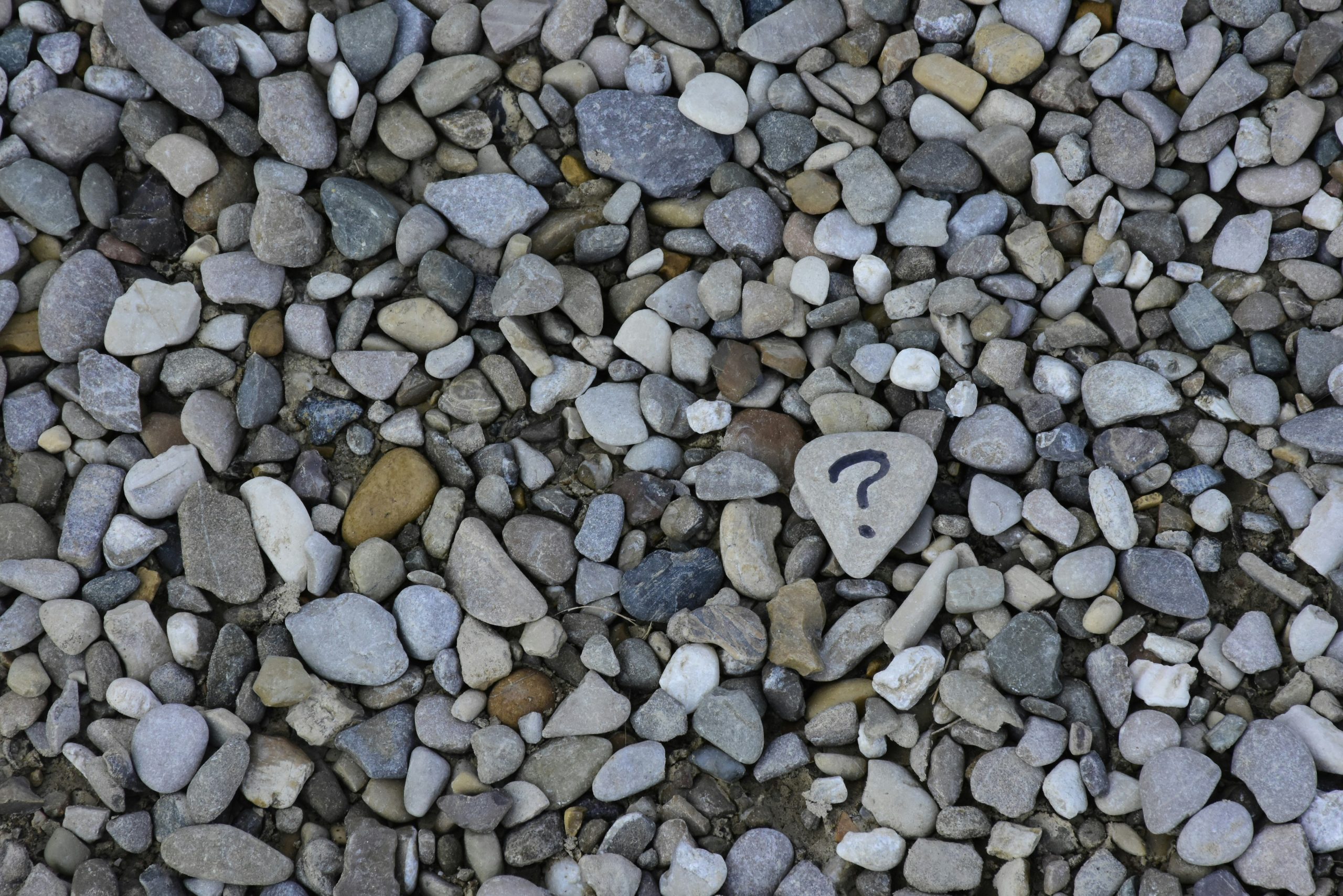 Ein Haufen Kieselsteine, auf einem großen flachen Stein ist ein Fragezeichen zu sehen