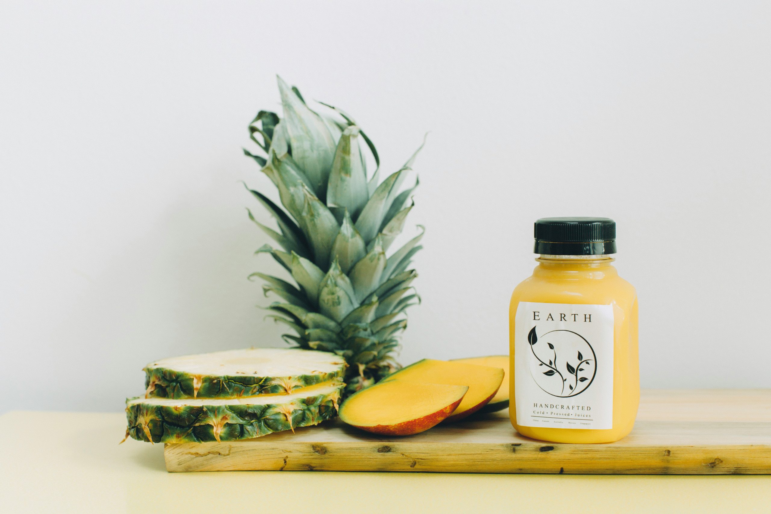 Ein Ananassaft-Fläschchen mit geschnittener Ananas daneben auf einem Holzbrett