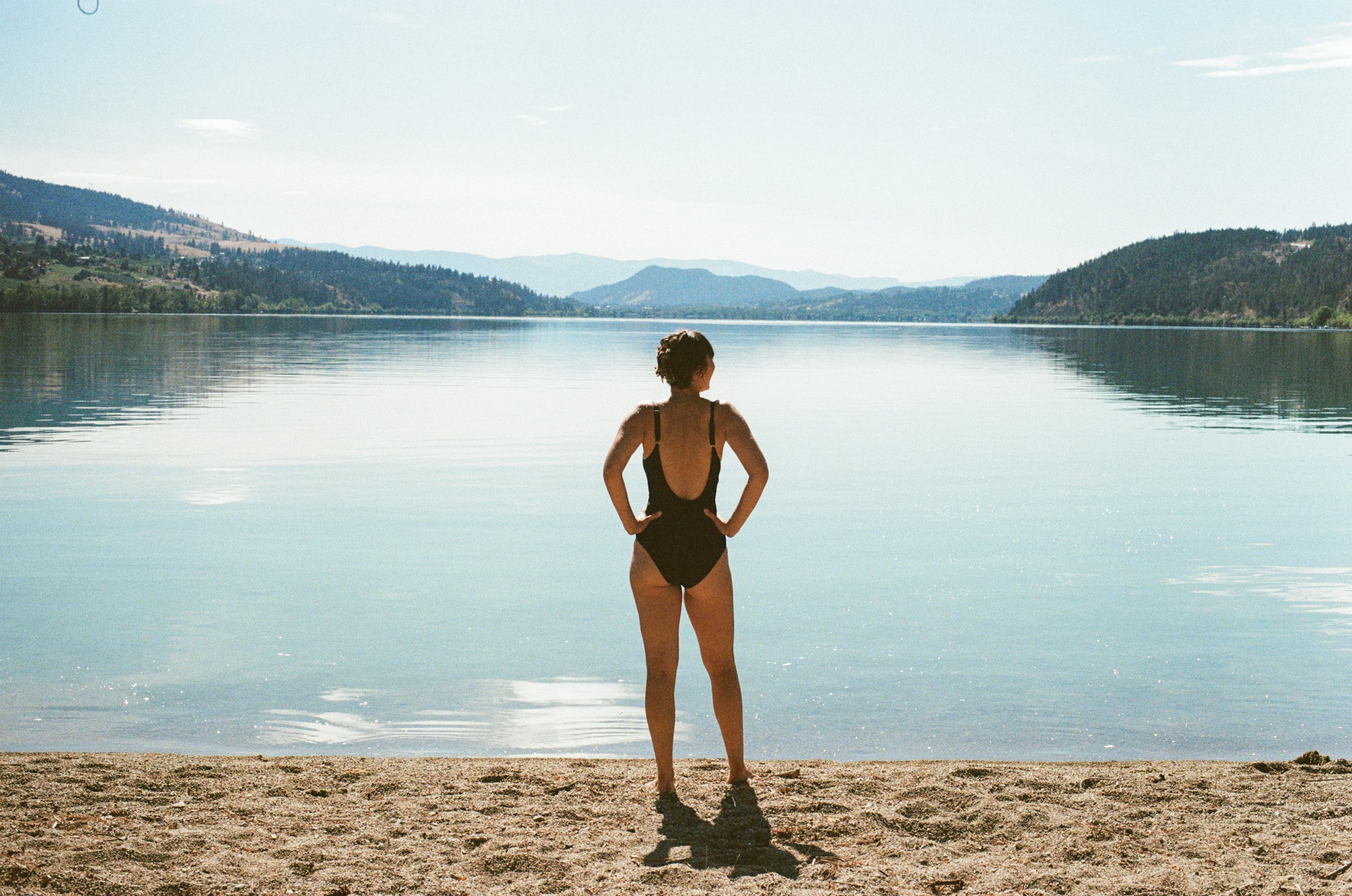 eine-frau-die-an-einem-strand-neben-einem-gewasser-steht-in-bademode-bikini