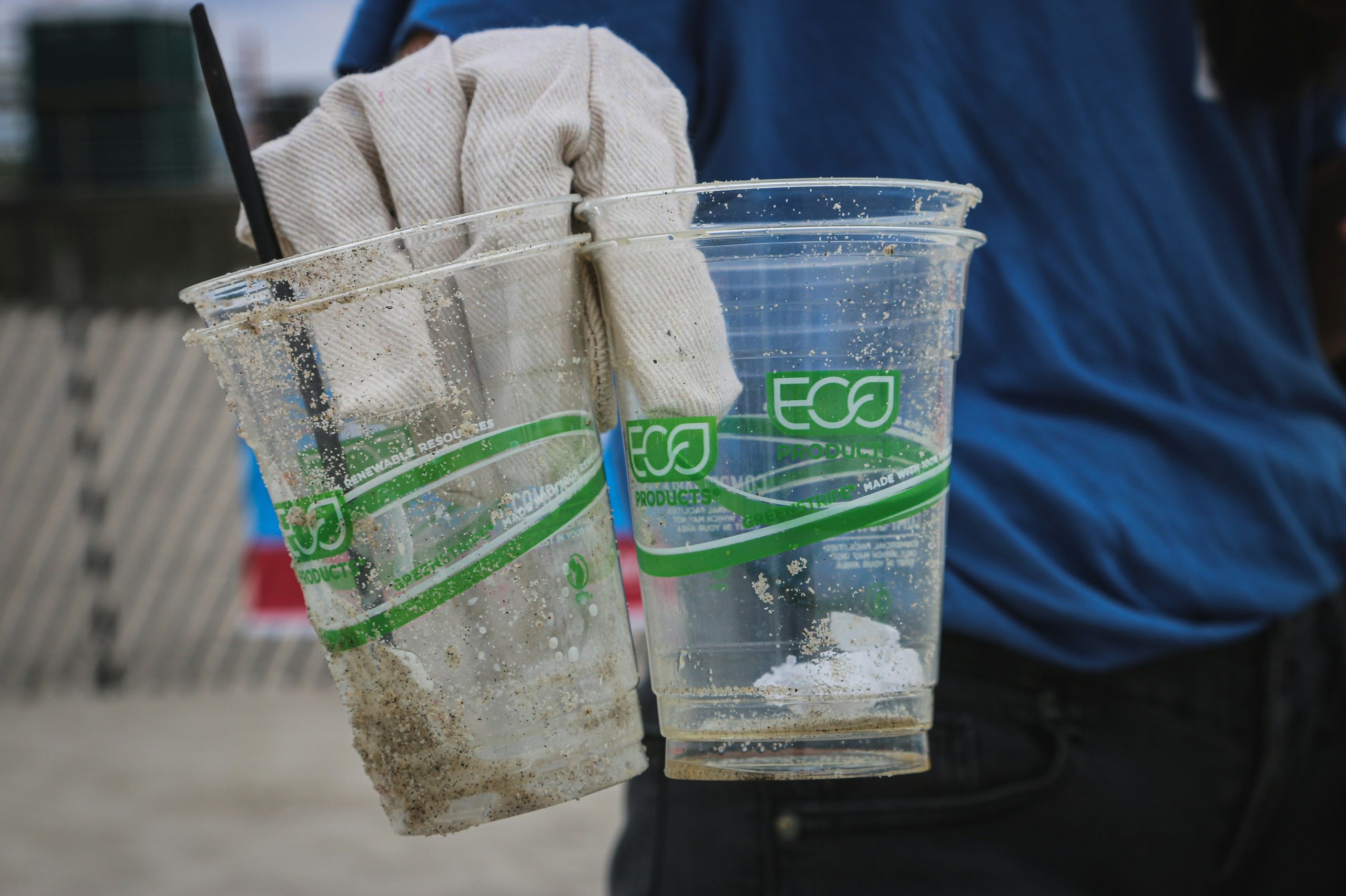 Plastikbecher mit grüner Eco-Aufschrift, die von Händen in Handschuhen gehalten werden